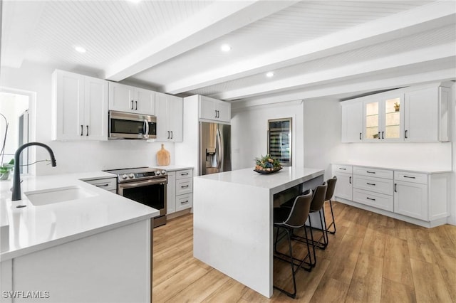 kitchen featuring light countertops, appliances with stainless steel finishes, white cabinetry, a kitchen island, and a kitchen bar