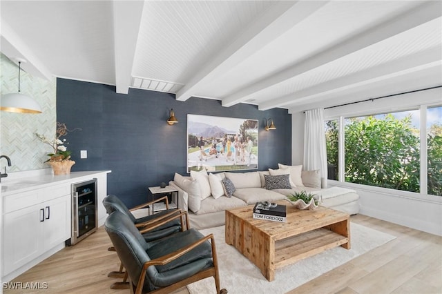 living area featuring beverage cooler, an accent wall, light wood finished floors, and beam ceiling