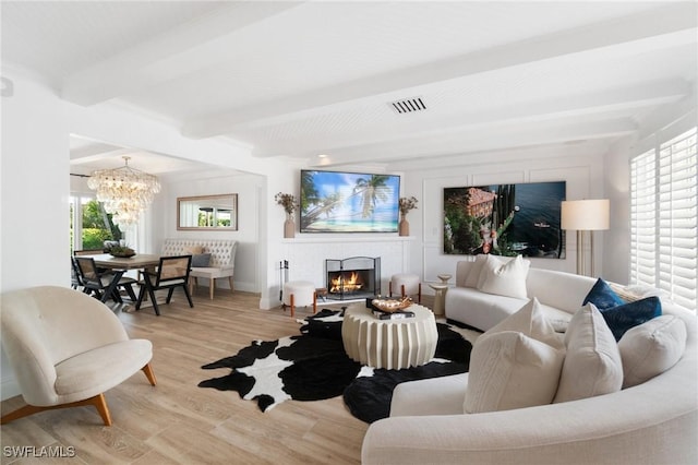 living area with a warm lit fireplace, visible vents, light wood-type flooring, a chandelier, and beam ceiling