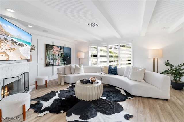 living room with light wood finished floors, beamed ceiling, a brick fireplace, and visible vents