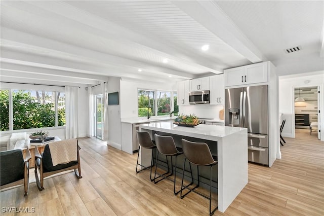 kitchen featuring visible vents, a kitchen island, a breakfast bar, stainless steel appliances, and white cabinetry