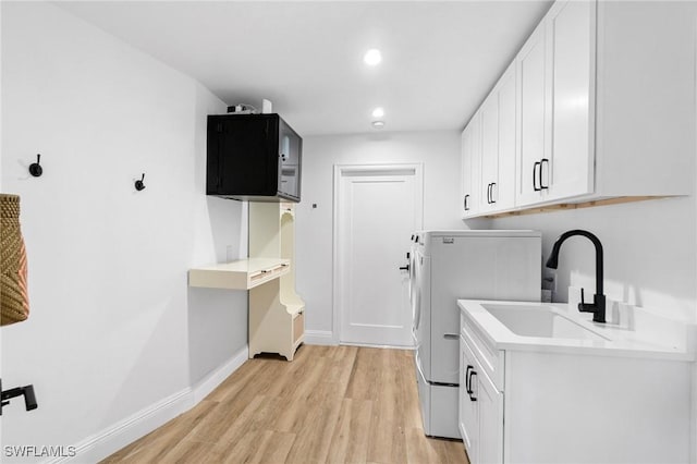 laundry room with cabinet space, baseboards, light wood-type flooring, a sink, and recessed lighting