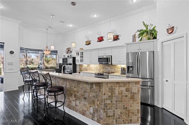 kitchen featuring a breakfast bar area, hanging light fixtures, ornamental molding, stainless steel appliances, and white cabinets