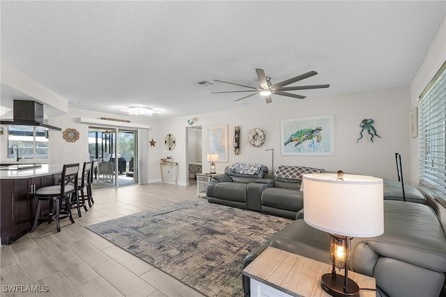 living room with ceiling fan, sink, a textured ceiling, and light hardwood / wood-style flooring