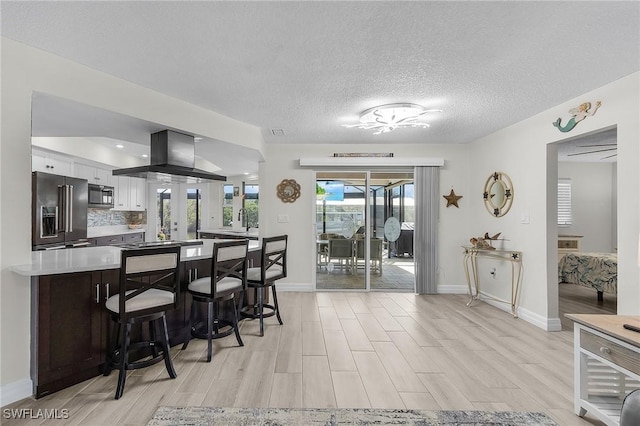 kitchen with tasteful backsplash, white cabinetry, island exhaust hood, light hardwood / wood-style floors, and high end fridge