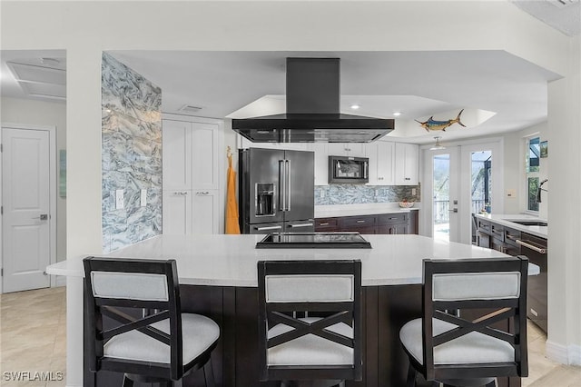 kitchen with a breakfast bar, tasteful backsplash, white cabinetry, island range hood, and black appliances