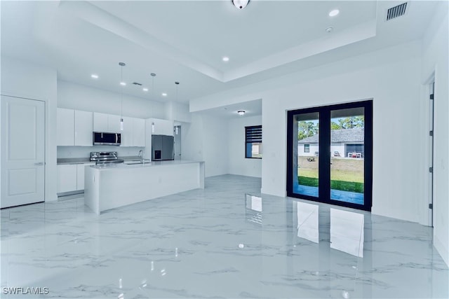 kitchen featuring pendant lighting, appliances with stainless steel finishes, a tray ceiling, an island with sink, and white cabinets