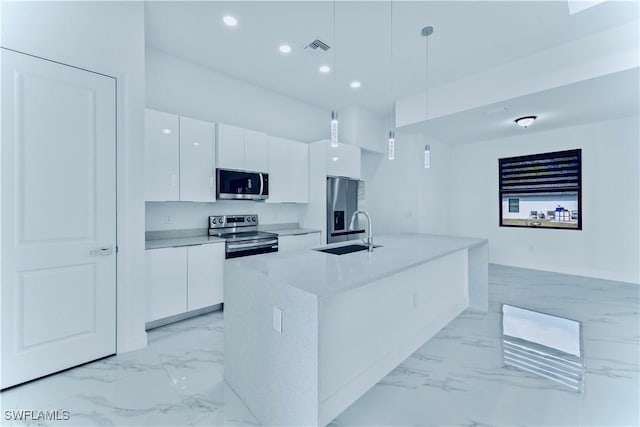 kitchen with pendant lighting, sink, appliances with stainless steel finishes, white cabinetry, and an island with sink