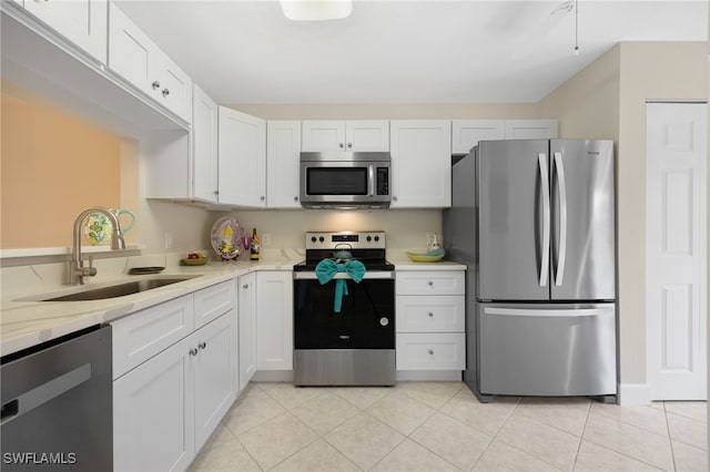 kitchen with sink, white cabinets, light tile patterned floors, light stone counters, and stainless steel appliances