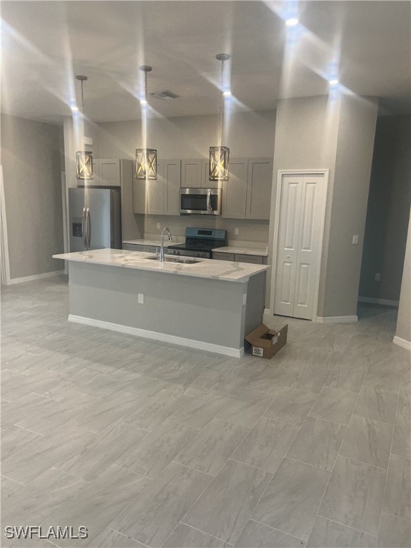 kitchen featuring sink, gray cabinets, appliances with stainless steel finishes, an island with sink, and decorative light fixtures