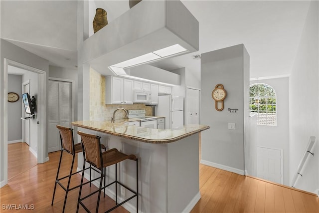 kitchen with white cabinetry, backsplash, white appliances, kitchen peninsula, and light wood-type flooring