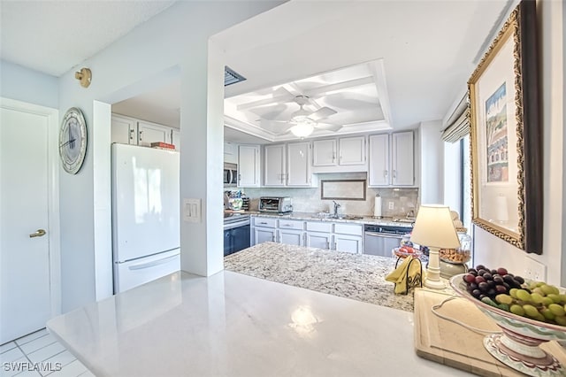 kitchen with sink, appliances with stainless steel finishes, a raised ceiling, ceiling fan, and backsplash