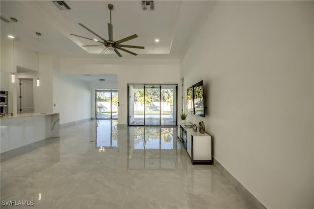 living room featuring a raised ceiling, a high ceiling, and ceiling fan