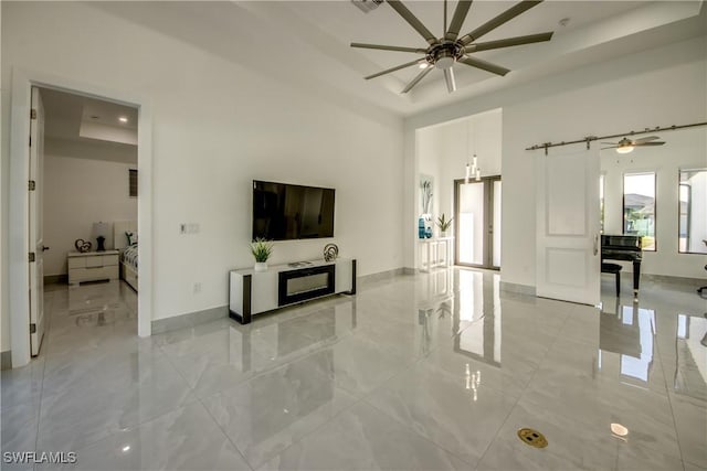 living room featuring a barn door, ceiling fan, and a tray ceiling