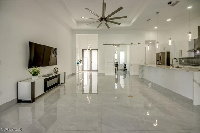 living room featuring sink, ceiling fan, a high ceiling, a tray ceiling, and a barn door