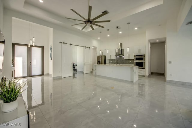 kitchen featuring white cabinetry, hanging light fixtures, wall chimney range hood, and a barn door