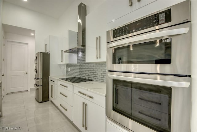 kitchen featuring appliances with stainless steel finishes, white cabinetry, backsplash, light stone countertops, and wall chimney exhaust hood