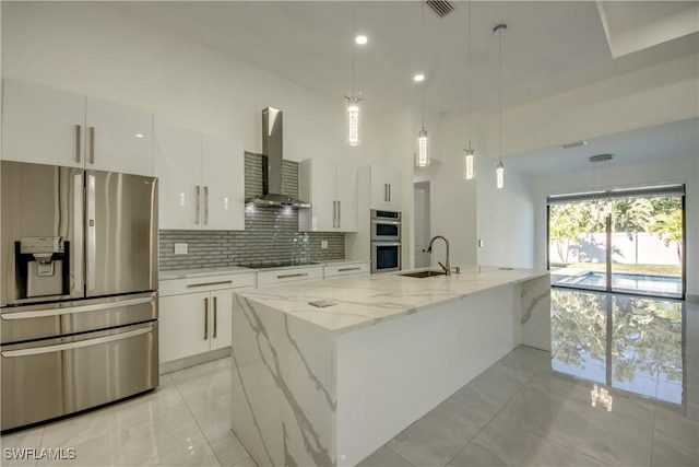 kitchen featuring a kitchen island with sink, wall chimney range hood, white cabinets, and appliances with stainless steel finishes