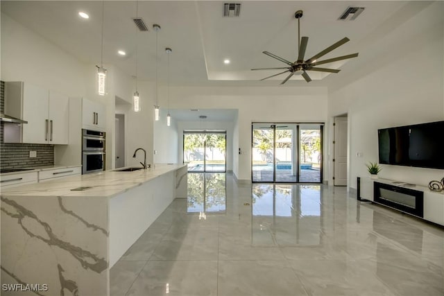 kitchen with sink, white cabinetry, light stone counters, decorative light fixtures, and a large island