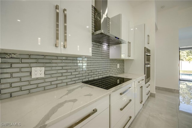 kitchen featuring tasteful backsplash, white cabinets, black electric stovetop, light stone countertops, and wall chimney range hood