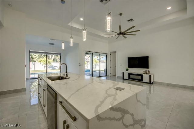 kitchen with sink, decorative light fixtures, a tray ceiling, a kitchen island with sink, and white cabinets