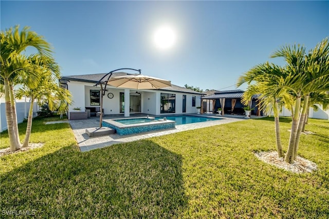 rear view of property featuring a swimming pool with hot tub, a lawn, and a patio