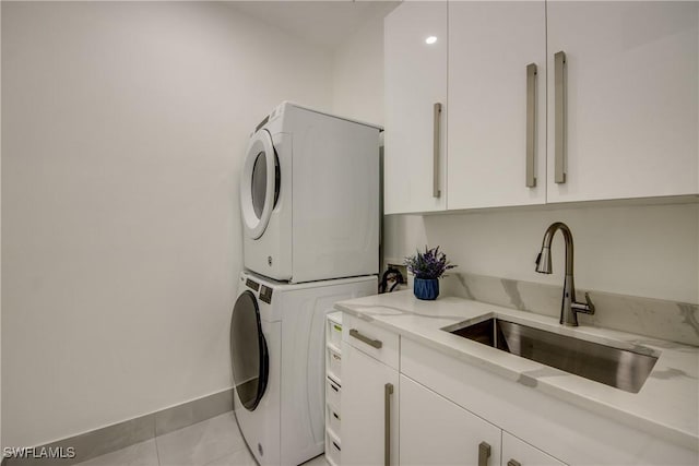 washroom featuring cabinets, light tile patterned flooring, stacked washer / drying machine, and sink