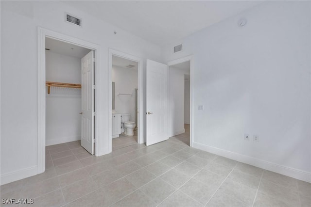 unfurnished bedroom featuring a walk in closet, connected bathroom, a closet, and light tile patterned floors