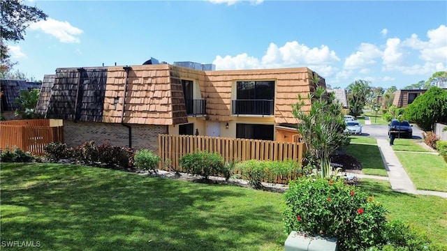 view of front of property featuring brick siding, fence, a front lawn, and mansard roof