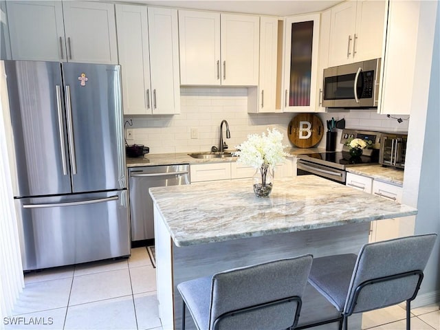 kitchen featuring light tile patterned floors, appliances with stainless steel finishes, a sink, and white cabinets