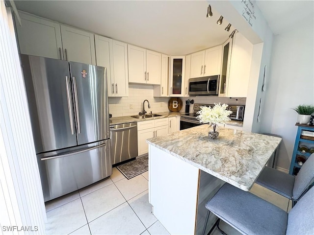 kitchen with light tile patterned floors, backsplash, appliances with stainless steel finishes, glass insert cabinets, and a sink