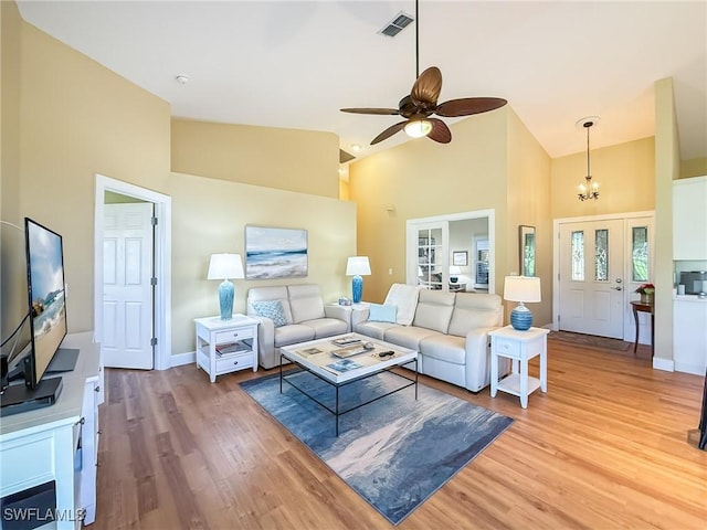 living room with ceiling fan with notable chandelier, high vaulted ceiling, and light hardwood / wood-style floors