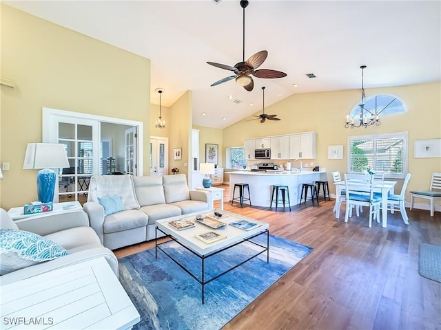 living room featuring dark hardwood / wood-style flooring, ceiling fan with notable chandelier, and high vaulted ceiling