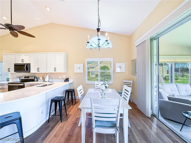 dining area with hardwood / wood-style floors, lofted ceiling, sink, and ceiling fan with notable chandelier