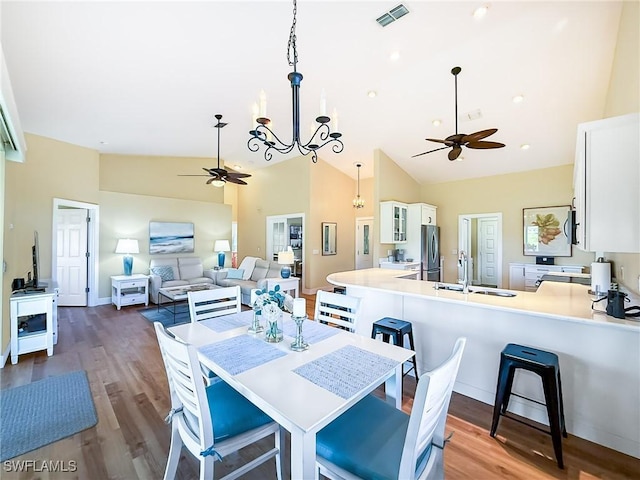 dining area with sink, ceiling fan with notable chandelier, dark wood-type flooring, and high vaulted ceiling