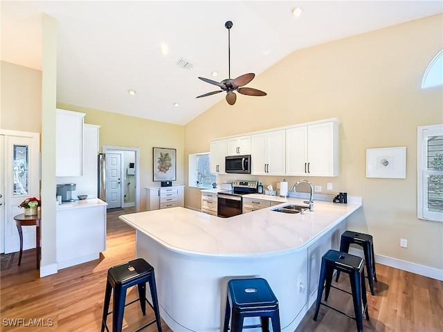 kitchen with stainless steel appliances, white cabinets, sink, a kitchen bar, and kitchen peninsula