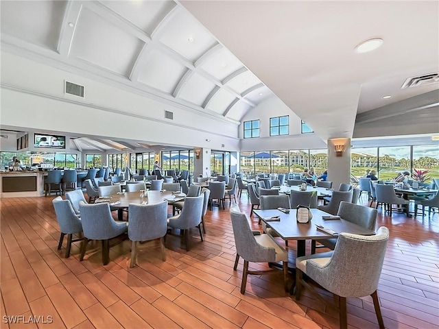 dining space with hardwood / wood-style floors, a healthy amount of sunlight, and high vaulted ceiling