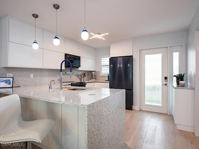 kitchen featuring white cabinets, freestanding refrigerator, a peninsula, black microwave, and a sink