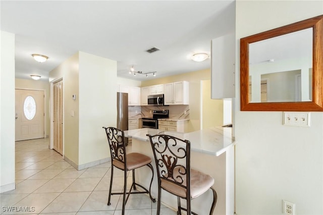 kitchen featuring a breakfast bar area, light tile patterned flooring, a peninsula, light countertops, and appliances with stainless steel finishes