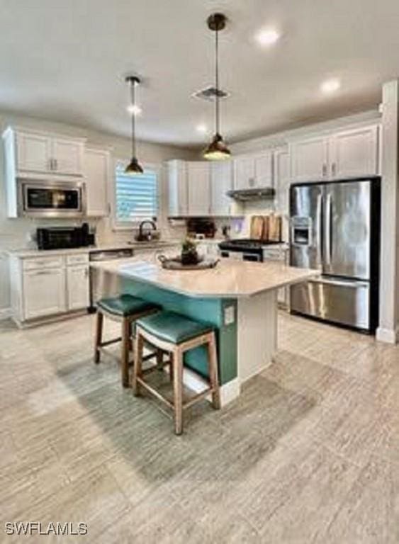 kitchen with pendant lighting, a breakfast bar, white cabinetry, stainless steel appliances, and a kitchen island