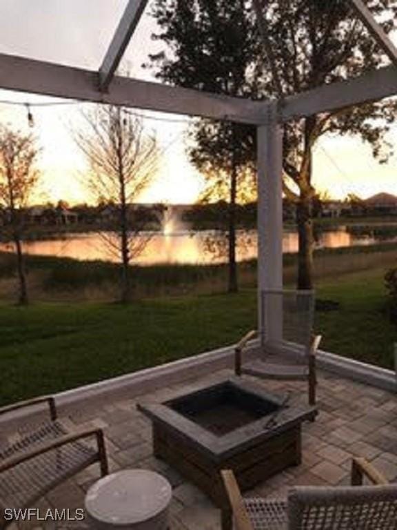 patio terrace at dusk featuring an outdoor fire pit, a lawn, and a water view