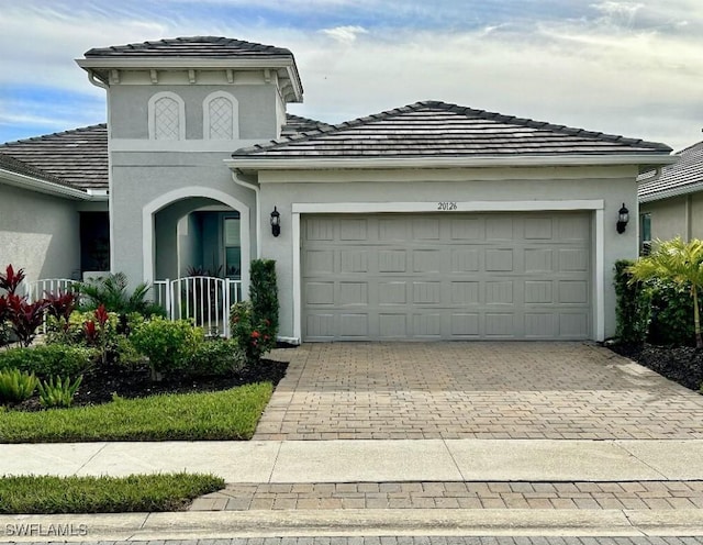 view of front facade featuring a garage, decorative driveway, a tiled roof, and stucco siding