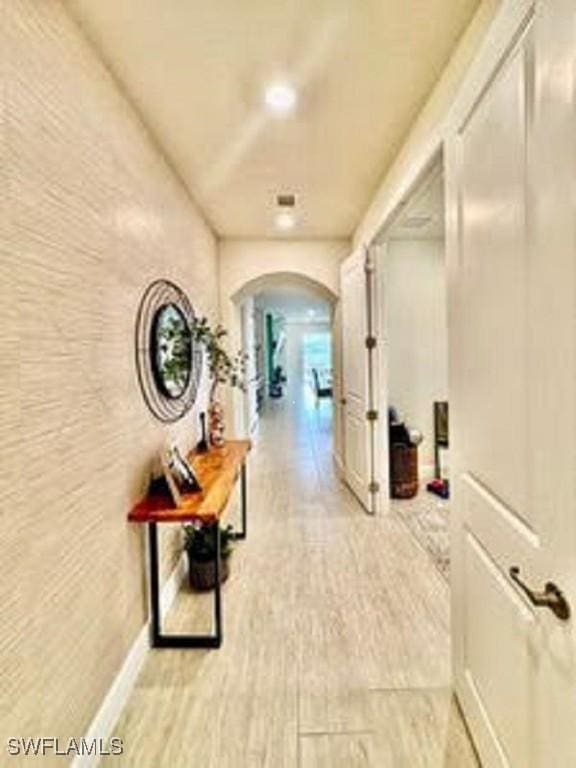 corridor featuring arched walkways, light wood-style flooring, and baseboards