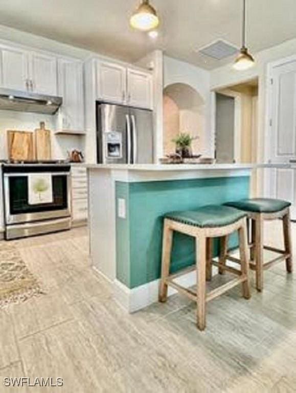 kitchen with a kitchen breakfast bar, hanging light fixtures, stainless steel appliances, light countertops, and under cabinet range hood