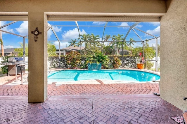 view of pool with a patio, pool water feature, a grill, and glass enclosure