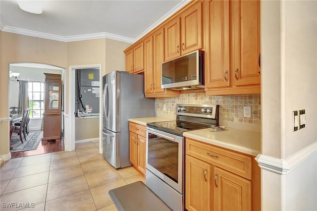 kitchen with light tile patterned floors, decorative backsplash, ornamental molding, and appliances with stainless steel finishes