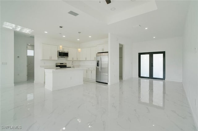 kitchen featuring appliances with stainless steel finishes, an island with sink, white cabinets, hanging light fixtures, and a tray ceiling