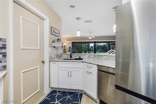 kitchen with sink, light stone counters, hanging light fixtures, stainless steel refrigerator, and white cabinets