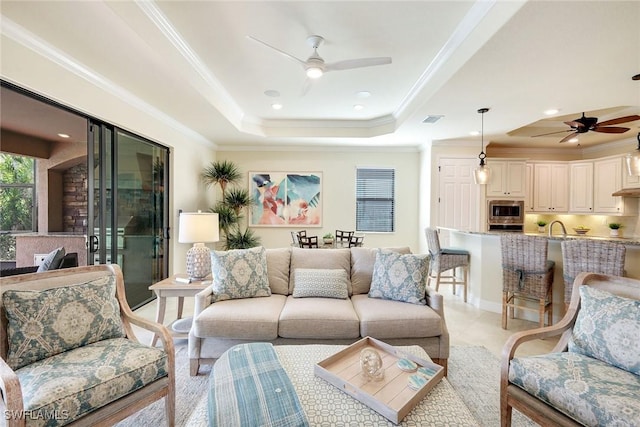 living room featuring ceiling fan, ornamental molding, a tray ceiling, and light tile patterned floors