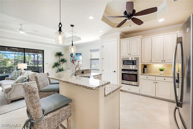 kitchen with appliances with stainless steel finishes, hanging light fixtures, a tray ceiling, light stone countertops, and a kitchen bar